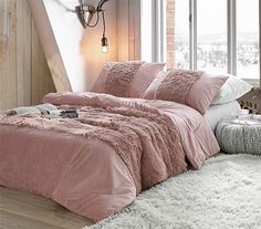 a bed with pink comforter and pillows in a room next to a window,