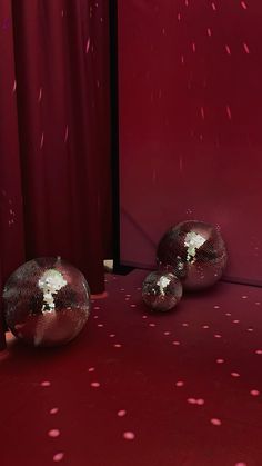 three shiny balls are on the floor in front of a red wall with white dots