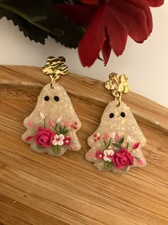 two earrings with flowers on them are sitting on a table next to a red flower