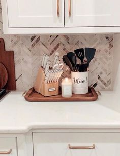 kitchen utensils on tray in front of white cabinets and marble backsplash