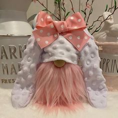 a pink and white stuffed animal with a bow on it's head sitting in front of a vase