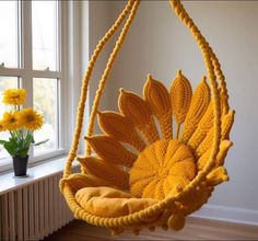 a knitted sunflower hanging chair next to a window with yellow flowers in the background