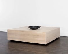 a black bowl sitting on top of a wooden table in a room with white walls