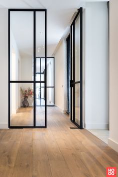 an empty hallway with wooden floors and black glass doors that lead into the living room