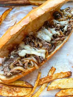 a sandwich with meat, cheese and onions on top of french fries sitting on a piece of parchment paper