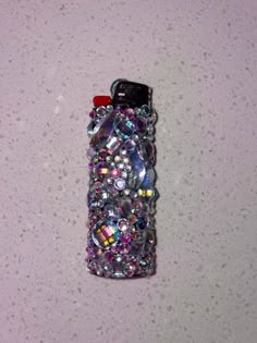 a cell phone covered in lots of different colored jewels on a white counter top next to a red object