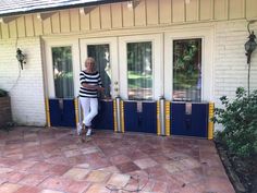 an older woman standing in front of a white house with blue and yellow striped doors