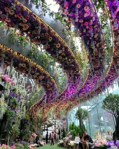 people are sitting on benches in the middle of an indoor garden area with flowers hanging from the ceiling