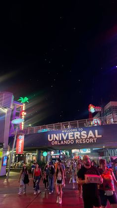 many people are walking around in front of the universal studios sign at night with bright lights