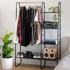 a rack with clothes and shoes on it next to a bed in a room filled with plants