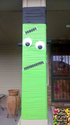 a tall green paper mache with eyes and teeth on it's face, standing in front of a house