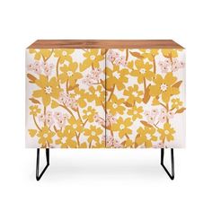 a yellow and white cabinet with flowers painted on the front, two black metal legs