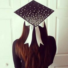 a woman wearing a black and white graduation cap with polka dots on the top, standing in front of a door