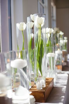 white tulips are in clear vases on a table with candles and napkins