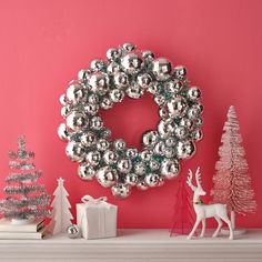 a christmas wreath on top of a mantel with silver ornaments and trees in the background