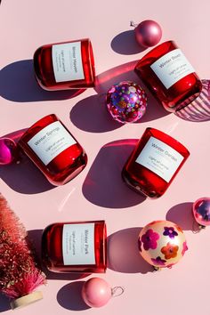 three red candles sitting on top of a pink surface next to christmas ornaments and baubles