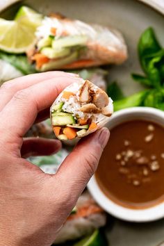 someone holding up a vegetable wrap with dipping sauce