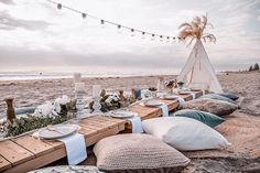 a table set up on the beach with pillows and blankets, plates and napkins