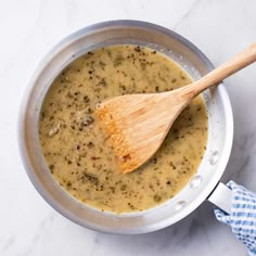 a wooden spoon in a pot filled with broccoli and cheese soup on a marble counter top