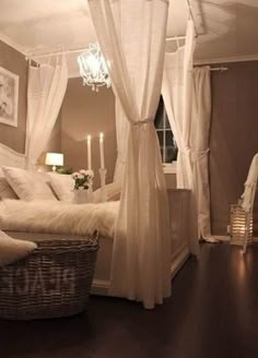 a bed with white sheets and curtains next to a chandelier in a bedroom