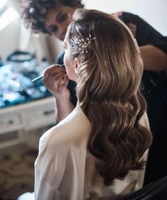 a woman is getting her hair done in the mirror while another person watches from behind