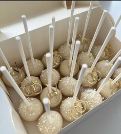 a box filled with wedding cake pops covered in white frosting and gold ring decorations