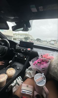 a woman sitting in the driver's seat of a car with two cups of coffee