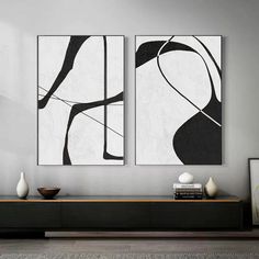 two black and white paintings hanging on the wall in a living room next to a coffee table