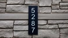 a house number sign mounted to the side of a stone wall