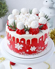 a red and white decorated cake on a table with christmas decorations around the edges,