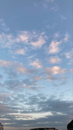 an airplane is flying in the sky with clouds above it and some buildings on the other side