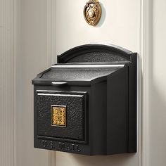 a black mailbox mounted to the side of a white door with a gold lion emblem on it