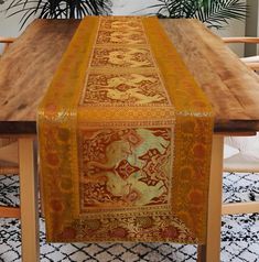 a long table with an intricately designed runner on it's end, sitting in front of a potted plant