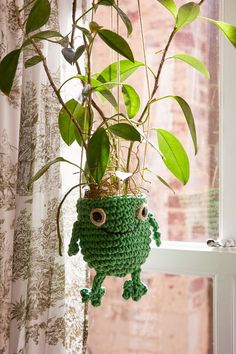 a crocheted green monster hanging from a window sill next to a potted plant