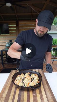 a man in black shirt cooking food on top of a wooden cutting board and table