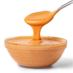 a wooden spoon is dipping sauce into a bowl