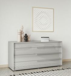 a white dresser with drawers and vases on it in front of a framed art piece