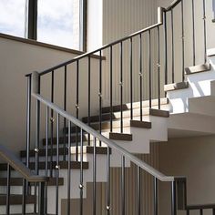 a stair case in front of a window next to a white wall and stairs with black handrails