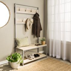 a room with a bench, coat rack and potted plant next to a window