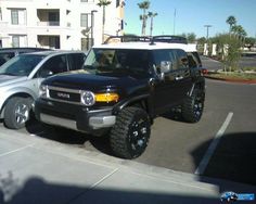 two suvs parked in a parking lot next to each other with palm trees behind them