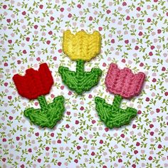 three crocheted flowers sitting on top of a pink and green table cloth covered surface