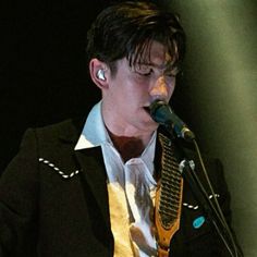 a young man singing into a microphone while wearing a black suit and gold neck tie