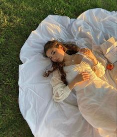 a woman laying on top of a white blanket in the grass next to an apple