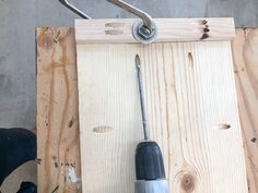 a drill is being held up by a wrench on a piece of plywood