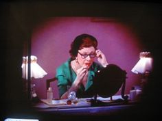 a woman sitting at a desk in front of a tv with her hand on her face