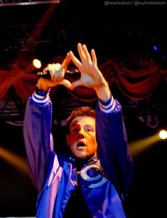 a male in a blue jacket is holding his hands up to the air while standing on stage