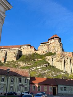 an old castle on top of a hill with cars parked in the parking lot below