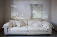 a white couch sitting next to a wall with clouds painted on the wall behind it