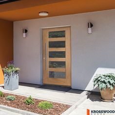 an orange umbrella is in front of a white building with a wooden door and planters