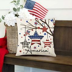 an american flag pillow sitting on top of a wooden bench next to a basket with flowers